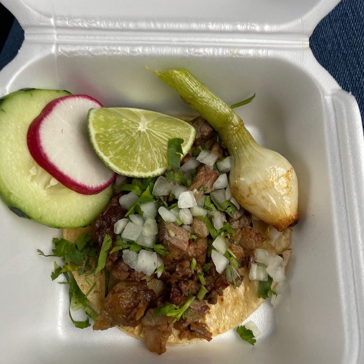 A taco with lime, radish, cucumber and a grilled onion in a foam box
