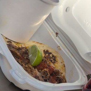 A taco with a lime wedge in a foam to-go box