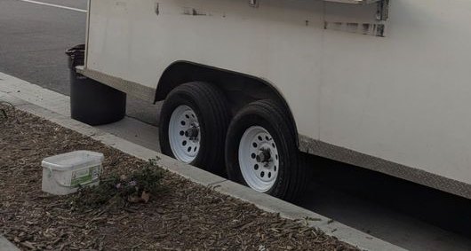The wheels of a white trailer parked by a curb, a folded-out steel shelf above
